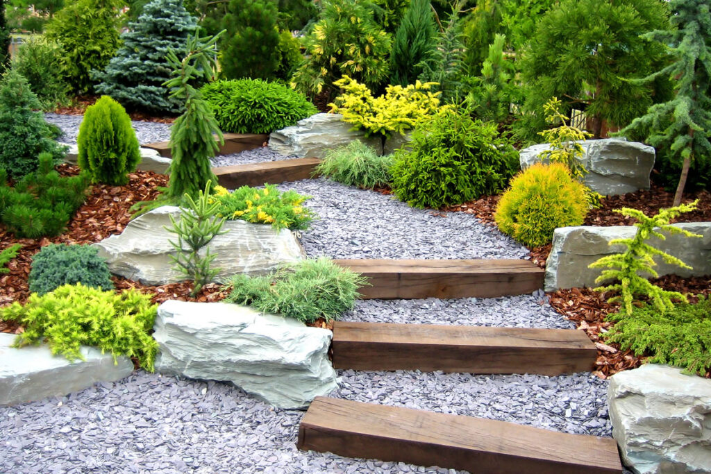 Hardscaped stairway with timber and gravel steps, boulders, and various evergreen plants