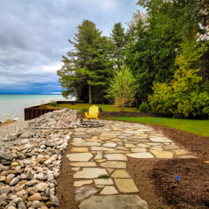 Lakefront landscaped back yard with flagstone sidewalk and patio, flower beds, and shoreline protection